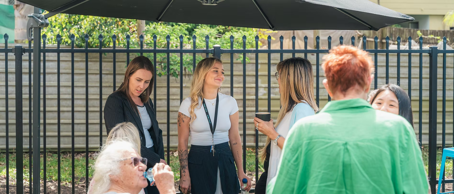 A diverse group of women chatting together outdoors under a shaded umbrella